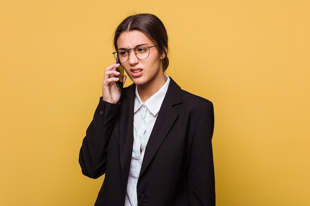 Mulher de negócios indiana jovem falando ao telefone isolado em fundo amarelo