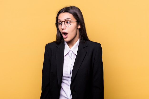 Mulher de negócios indiana jovem isolada em um fundo amarelo, sendo chocada por causa de algo que ela viu.