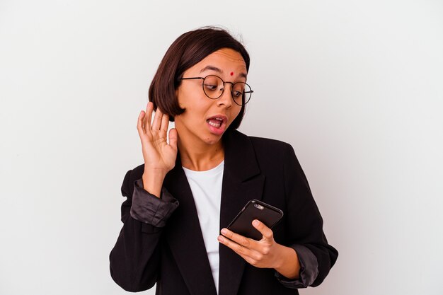 Mulher de negócios indiana jovem segurando um telefone isolado, tentando ouvir uma fofoca.