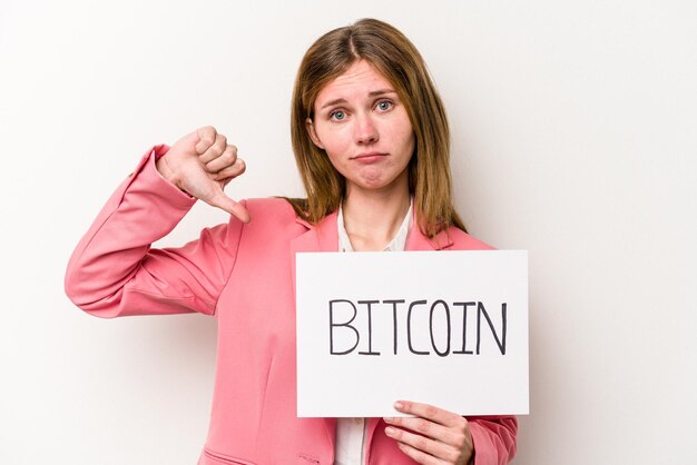 Mulher de negócios inglesa jovem segurando um cartaz de bitcoin isolado no fundo branco, mostrando um gesto de desagrado, polegares para baixo. Conceito de desacordo.