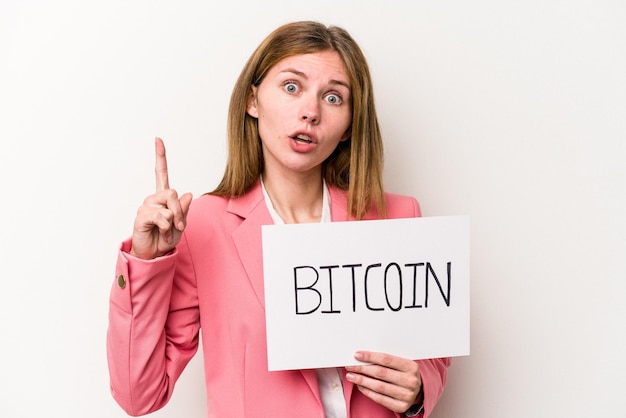 Mulher de negócios inglesa jovem segurando um cartaz de bitcoin isolado no fundo branco, tendo uma ideia, conceito de inspiração.