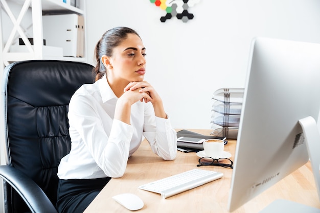 Mulher de negócios inteligente concentrada olhando para a tela do computador enquanto está sentada na mesa do escritório