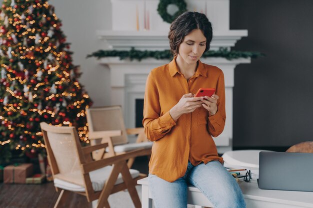 Mulher de negócios italiana atraente trabalhando em casa durante as férias de Natal usando um smartphone moderno