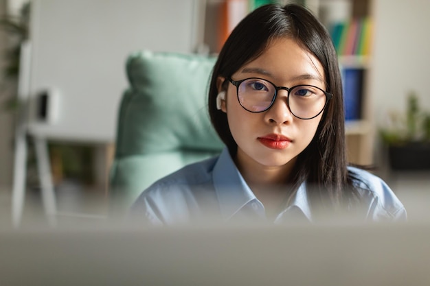 Mulher de negócios japonesa usando fones de ouvido usando computador no local de trabalho interno