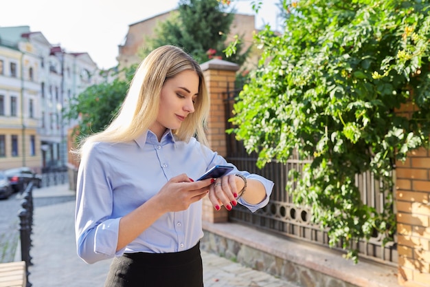 Mulher de negócios jovem ao ar livre com smartphone olhando para o relógio de pulso