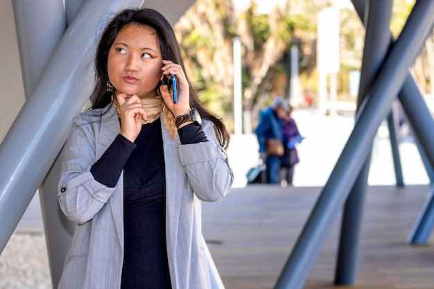 Mulher de negócios jovem asiática duvidosa falando no celular fazendo ligação trabalhando olhando para longe
