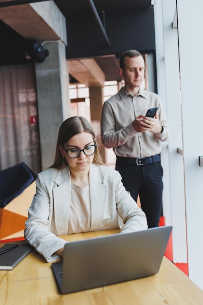 Mulher de negócios jovem atrás de um laptop usando óculos sentado em uma mesa tendo uma reunião de negócios corporativos com colegas em um escritório moderno Conceito de carreira empresarial Foco seletivo de espaço livre