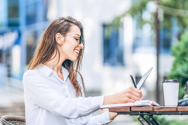 Mulher de negócios jovem bebendo café e trabalhando em um tablet no café de rua.