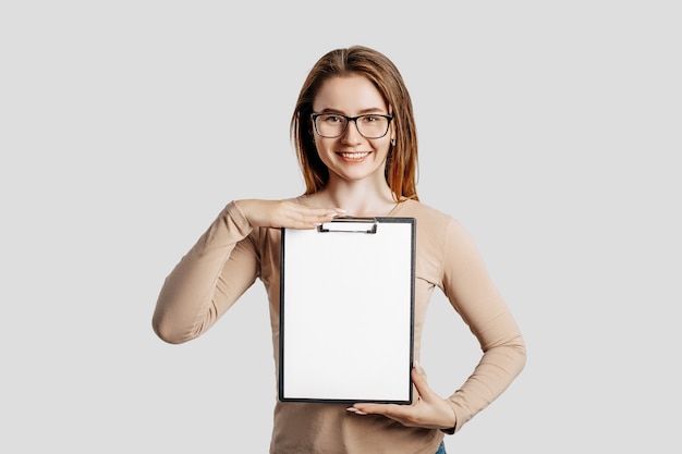 Foto mulher de negócios jovem bonita de óculos segura uma prancheta com simulação de espaço em branco isolado no fundo cinza. atingir o conceito de negócio de riqueza de carreira. capa de aprendizagem online