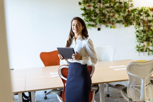 Mulher de negócios jovem com tablet digital em pé no escritório moderno