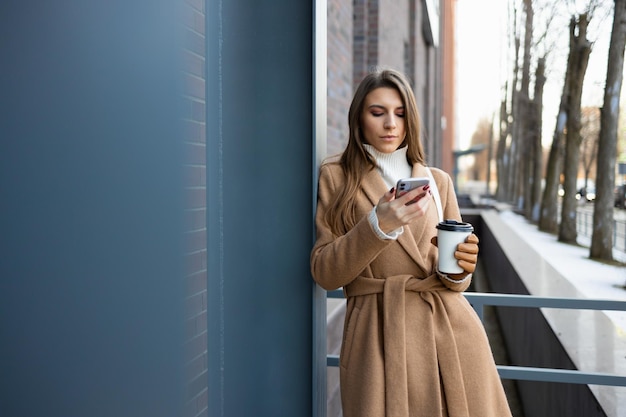 Mulher de negócios jovem elegante fica perto do prédio com smartphone