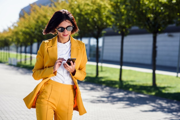 Mulher de negócios jovem elegante usa smartphone enquanto caminha perto do centro de negócios