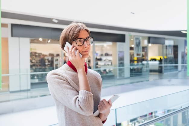 Mulher de negócios jovem falando ao telefone em um shopping center. Mulher com roupas casuais elegantes em loja de departamentos segurando um tablet