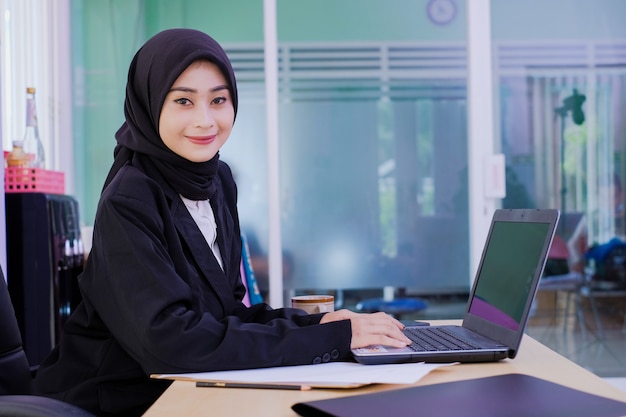 Mulher de negócios jovem feliz confiante sentada na mesa do escritório trabalhando no computador