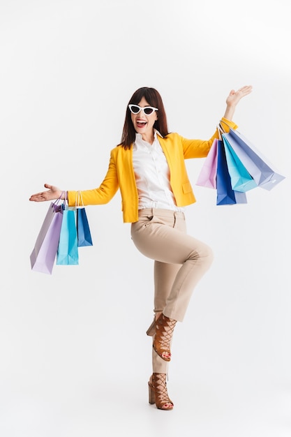 mulher de negócios jovem feliz linda posando isolada sobre uma parede branca, segurando sacolas de compras.