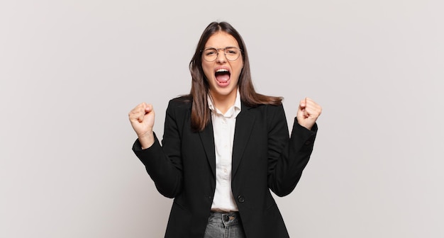 Mulher de negócios jovem gritando agressivamente com uma expressão de raiva ou com os punhos cerrados comemorando o sucesso