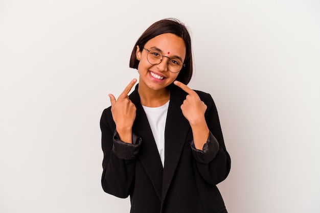 Mulher de negócios jovem indiana isolada em sorrisos de parede branca, apontando os dedos na boca.