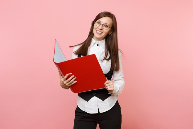 Mulher de negócios jovem linda morena bem-sucedida em copos, segurando uma pasta vermelha para documentos de documentos isolado no fundo rosa. Senhora chefe. Riqueza de carreira de realização. Copie o espaço para anúncio.