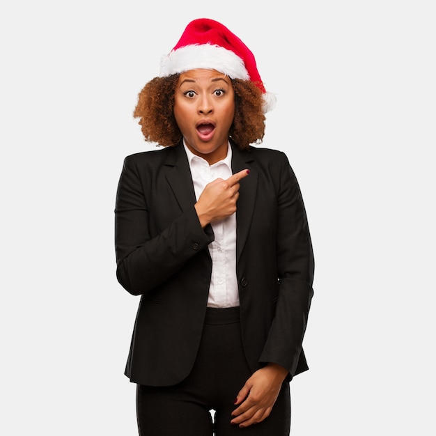 Mulher de negócios jovem negra usando um chapéu de Papai Noel chirstmas apontando para o lado