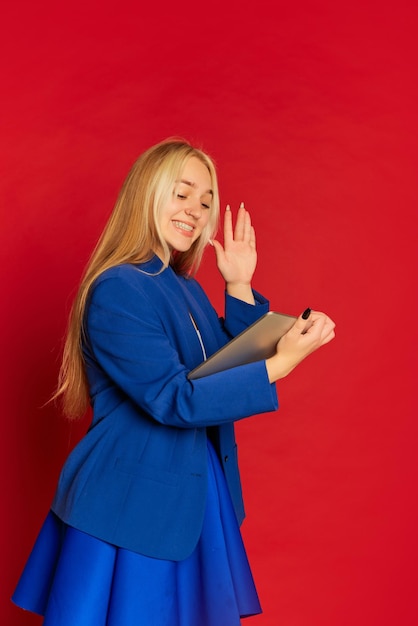 Mulher de negócios jovem positiva ou estudante feliz vestindo terno azul posando sobre fundo vermelho brilhante Conceito de realização de emoções de carreira de motivação de inicialização