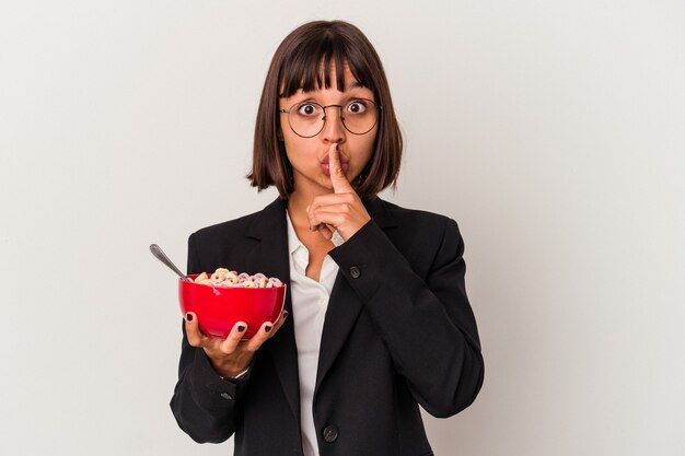 Mulher de negócios jovem raça mista comendo cereais isolados no fundo branco, mantendo um segredo ou pedindo silêncio.