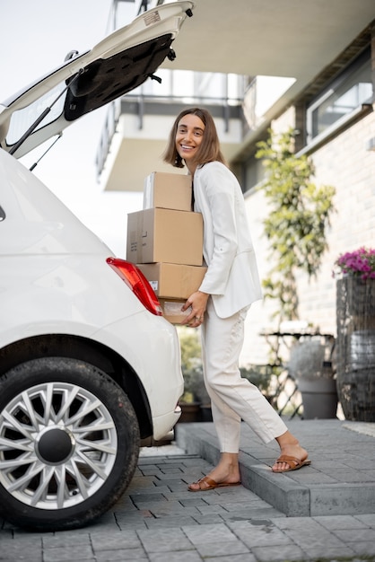 Foto mulher de negócios jovem recolhendo pacotes no porta-malas de um carro, voltando para casa de carro. conceito de comprar produtos online e entregá-los em casa