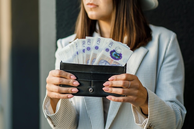 Mulher de negócios jovem segurando carteira preta com libras nas mãos close-up de mãos femininas O conceito de economia e salários de pagamentos em dinheiro