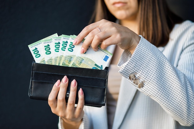 Mulher de negócios jovem segurando carteira preta com notas de euro close-up de mãos femininas com dinheiro O conceito de poupança e salários de pagamentos em dinheiro