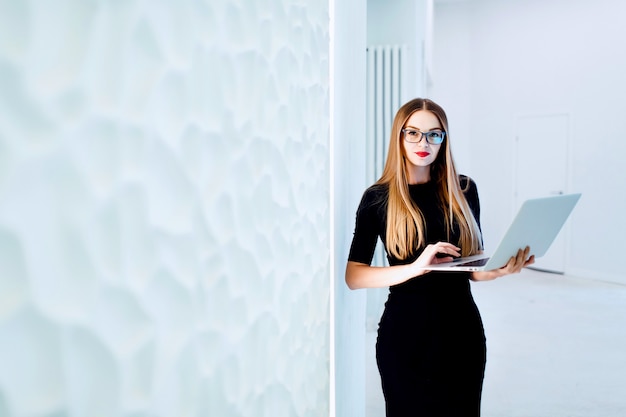 Mulher de negócios jovem segurando o computador nas mãos. fundo de escritório branco com espaço de cópia. tonificado