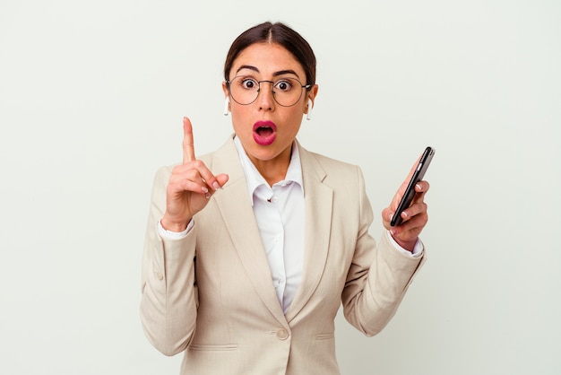 Mulher de negócios jovem segurando um telefone celular isolado na parede branca, tendo uma ideia, o conceito de inspiração.