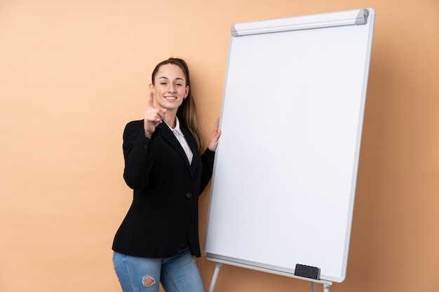 Mulher de negócios jovem sobre parede isolada, dando uma apresentação no quadro branco