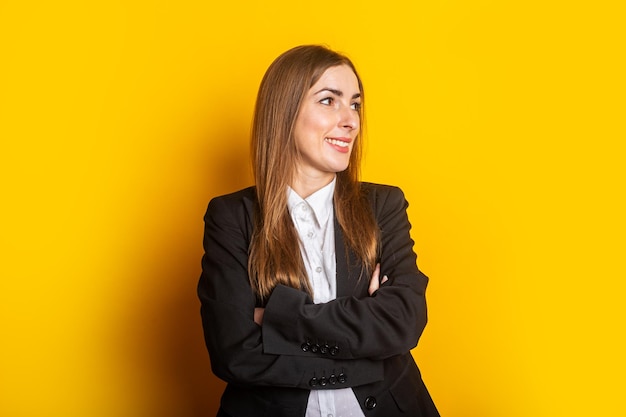 Mulher de negócios jovem sorridente em uma jaqueta preta olha para o lado em um fundo amarelo