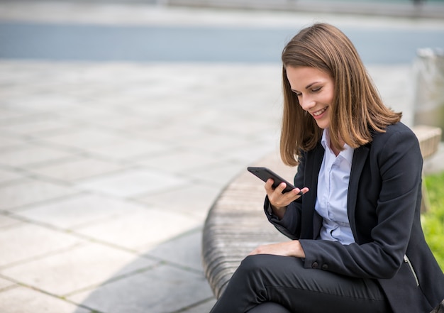 Mulher de negócios jovem sorridente usando seu telefone celular móvel