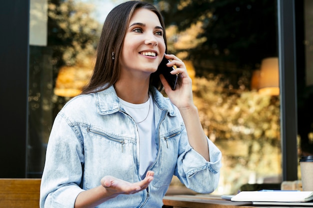 Mulher de negócios jovem trabalhando em um café no terraço aberto, sentado em frente ao laptop, falando ao telefone.