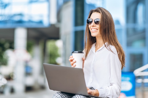 Mulher de negócios jovem trabalhando no laptop ao ar livre perto do centro de negócios.