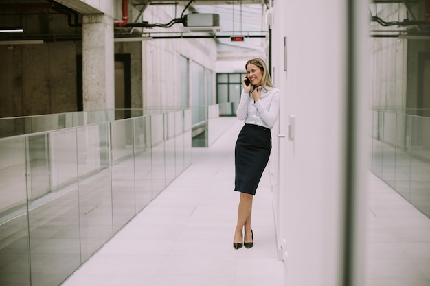 Mulher de negócios jovem usando telefone celular no corredor do escritório
