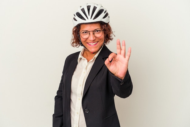 Mulher de negócios latinos de meia-idade usando um capacete de bicicleta isolado no fundo branco alegre e confiante mostrando o gesto de ok.