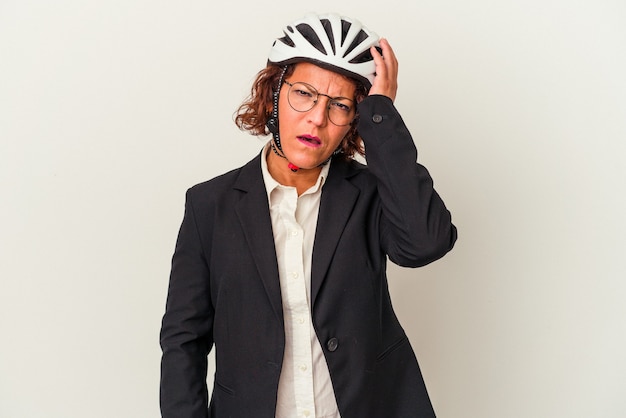 Mulher de negócios latinos de meia-idade usando um capacete de bicicleta isolado no fundo branco sendo chocada, ela se lembrou de uma reunião importante.