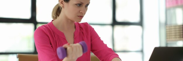 Mulher de negócios levantando halteres e trabalhando no laptop no escritório