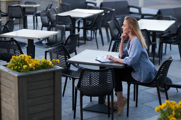 Mulher de negócios loira atraente está pensando em seu trabalho enquanto está sentado na cafeteria do lado de fora com a papelada.