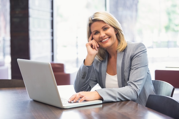 Mulher de negócios loira sorrindo usando laptop