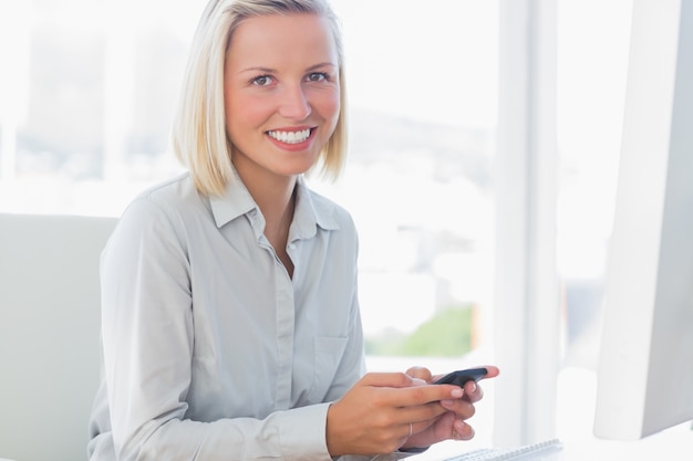 Mulher de negócios loira texting e sorrindo na câmera