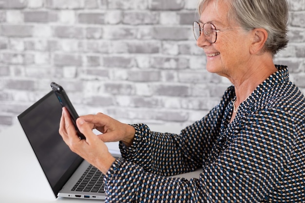 Mulher de negócios mais velha confiante sorridente trabalhando no laptop enquanto estiver usando o celular