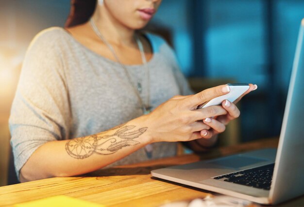 Mulher de negócios mãos e telefone no escritório à noite com digitação de mensagem de texto leitura notificação ou bate-papo móvel Funcionário profissional ou técnico com laptop na mesa para rolagem de mídia social em horas extras
