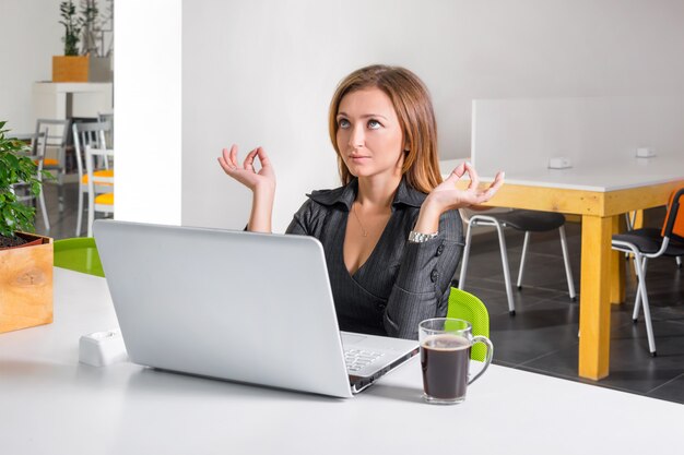 Mulher de negócios, meditando perto de laptop. Trabalhador de escritório relaxado fazendo yoga meditação durante uma pausa para café