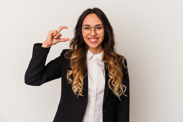 Mulher de negócios mexicana jovem isolada no branco segurando algo pequeno com os indicadores, sorrindo e confiante.