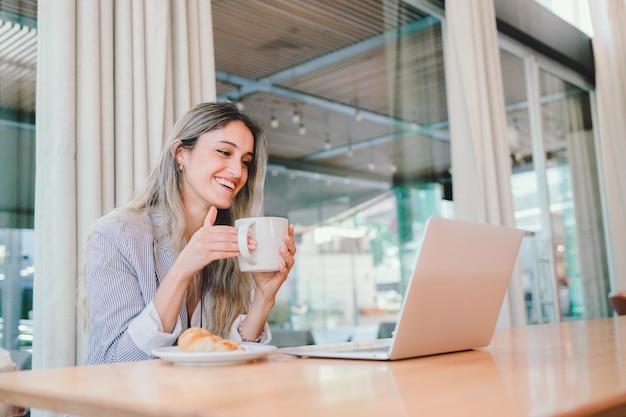 Mulher de negócios milenar pacífica usando laptop, com caneca de café no local de trabalho moderno.