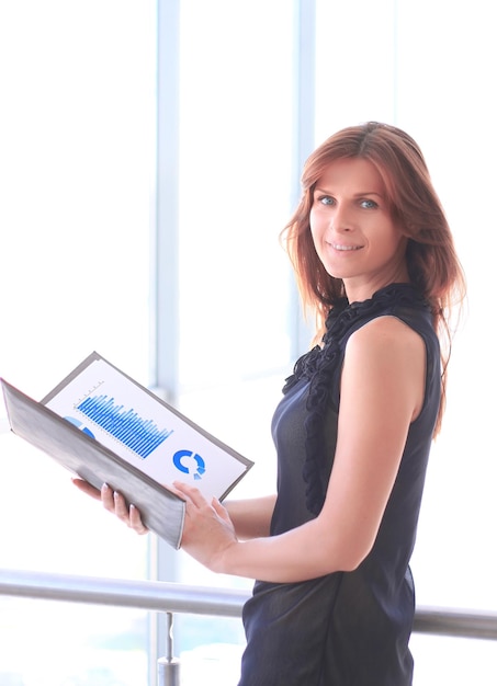 Mulher de negócios moderna com gráficos financeiros em pé perto de uma grande janela de escritório