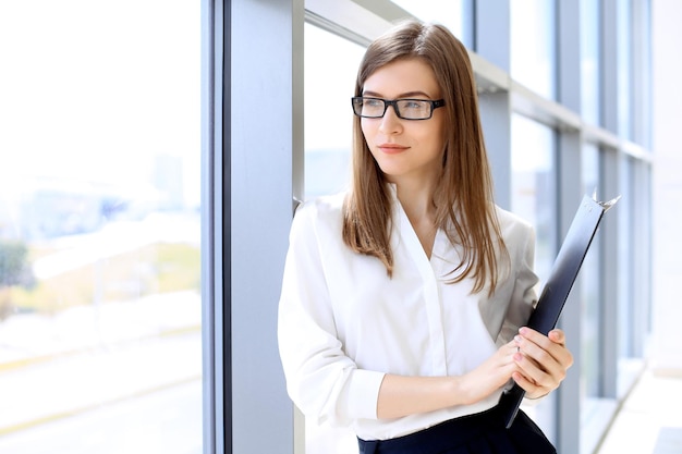 Mulher de negócios moderna em pé e mantendo papéis no escritório com área de espaço de cópia