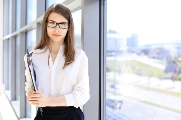 Mulher de negócios moderna em pé e mantendo uma prancheta no escritório